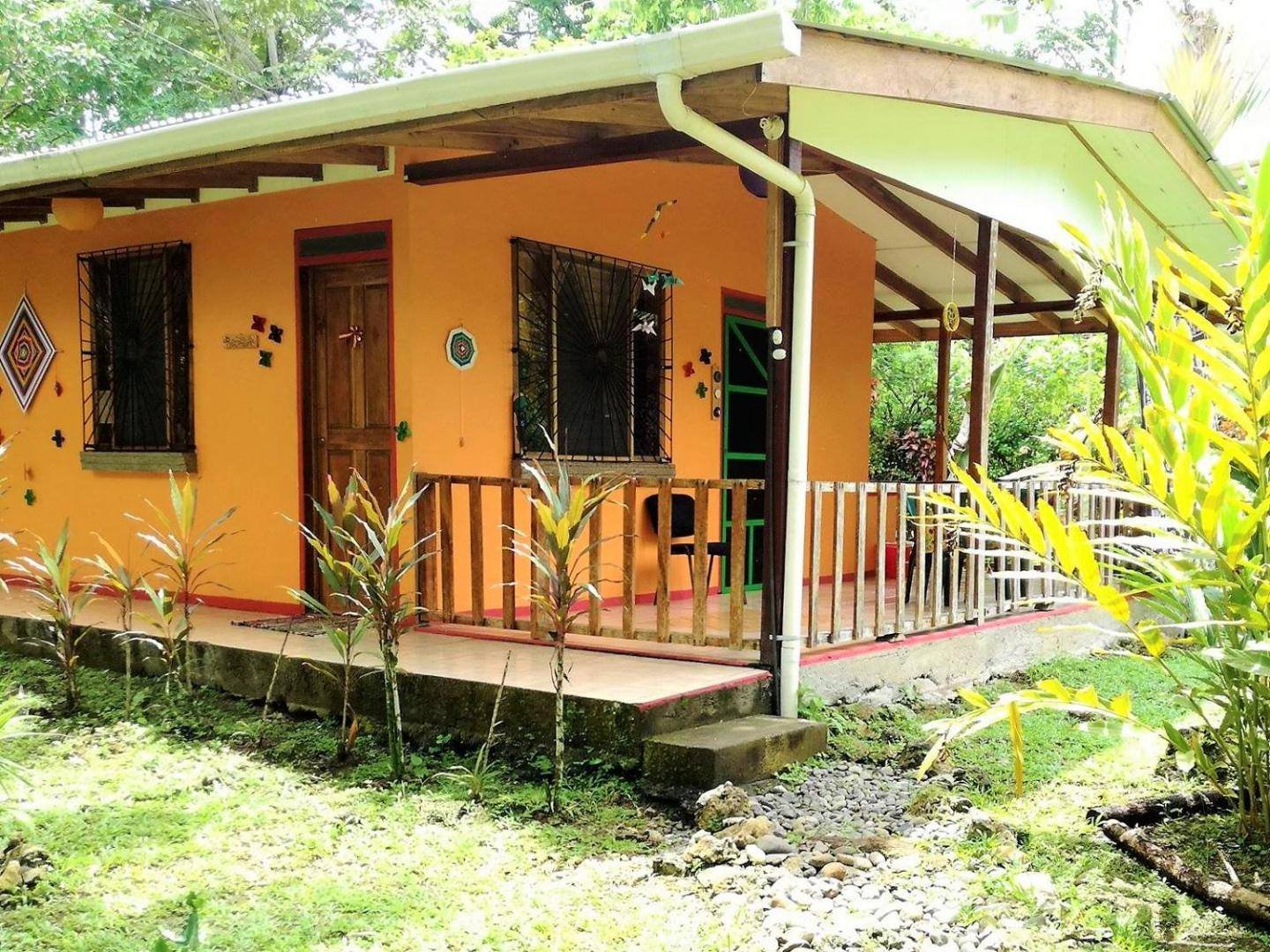 Orange cabin with a wooden porch surrounded by plants